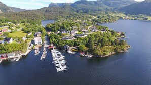 Luftaufnahme eines Dorfes am Seeufer mit Häusern, einem Yachthafen und Bergen im Hintergrund.