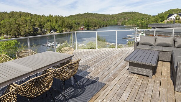 Eine Holzterrasse mit Gartenmöbeln, mit Blick auf einen Fluss und bewaldete Hügel.