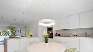 Una cocina moderna con armarios blancos, un salpicadero de mármol y una mesa de comedor redonda con sillas verdes.