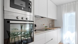 Una cocina moderna con electrodomésticos integrados, un comedor con mesa y sillas de vidrio, y vistas al exterior a través de cortinas translúcidas.