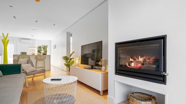 Una sala de estar moderna con chimenea, un televisor montado en la pared y un comedor al fondo.