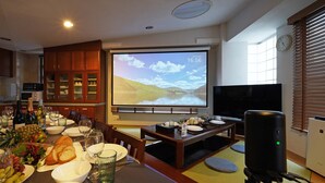 Un espace repas équipé d’un écran de projection diffusant un paysage pittoresque, d’un téléviseur et d’un haut-parleur.