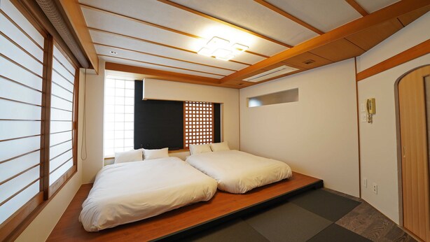 Une pièce avec un lit sur une plateforme basse, des poutres en bois, un luminaire au plafond, une cloison noire et une porte coulissante.