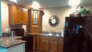 A kitchen with wooden cabinets, a black refrigerator, a stainless steel sink, and a wall clock. - Lake Road Cabin C — Million Dollar Ozark View! (Ironton)