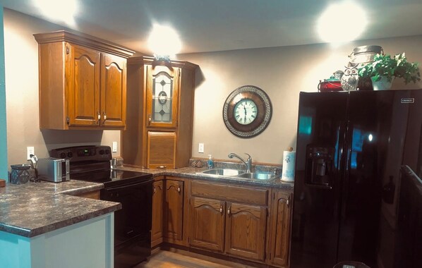 A kitchen with wooden cabinets, a black refrigerator, a stainless steel sink, and a wall clock.
