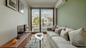 A modern living room with a sofa, a coffee table, a TV, and a large window offering a city view. - Legacy Oporto Premium Apartment C by Vacationy (Porto)
