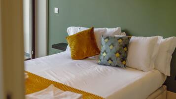 Un lit bien fait, avec du linge de lit blanc, un plaid de couleur moutarde et des coussins à motifs.