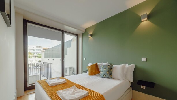 A modern hotel room with a large bed, a green accent wall, and a balcony with outdoor seating. - Legacy Oporto Premium Apartment C by Vacationy (Porto)