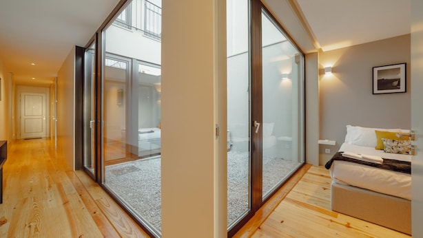 A modern bedroom with a large sliding glass door leading to a balcony, a bed with white bedding, and a small bedside table. - Legacy Oporto Premium Apartment B by Vacationy (Porto)