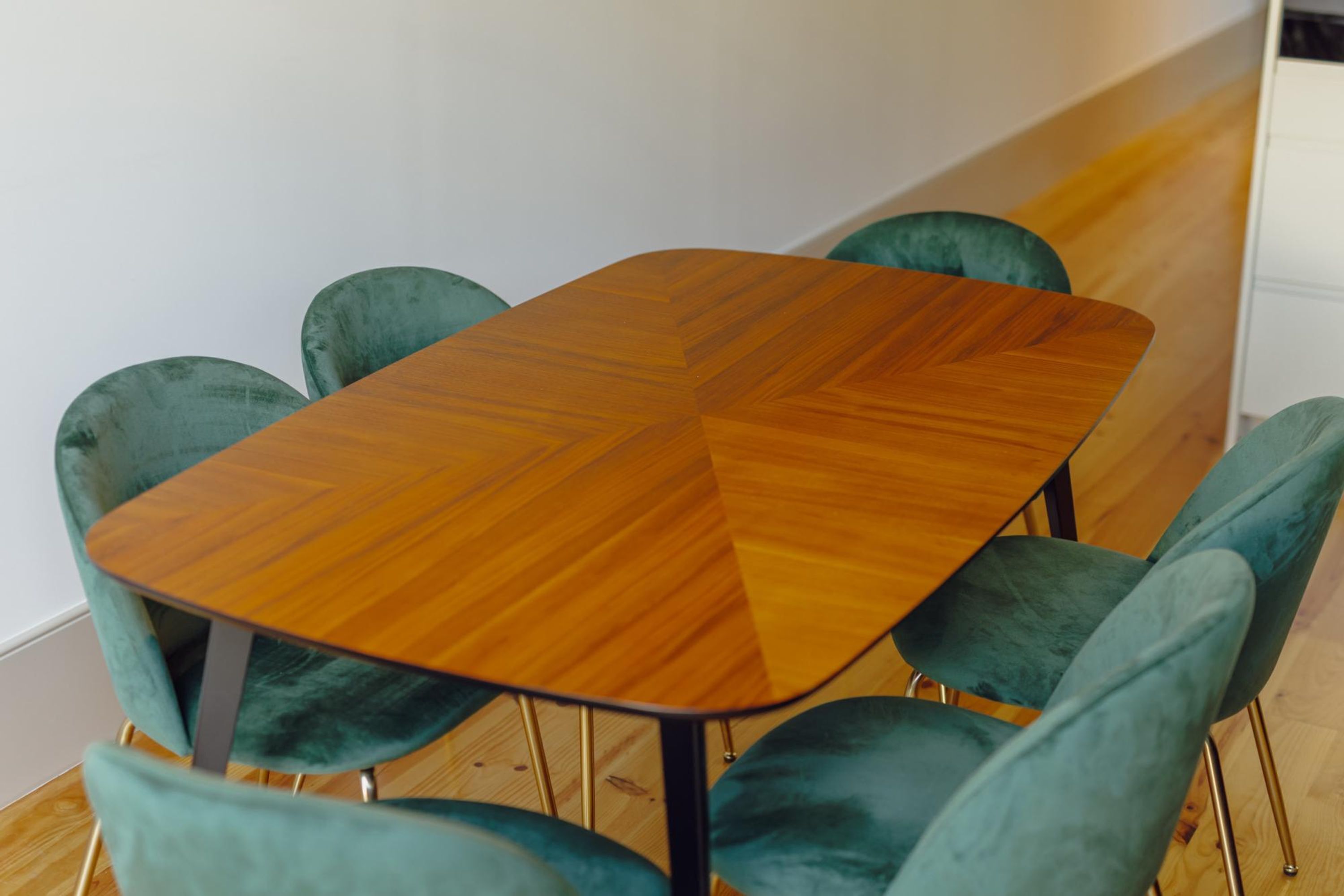 A dining table with a wooden surface and metal legs, surrounded by four green upholstered chairs.