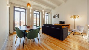 A spacious living area with a wooden floor, a dining table with chairs, a black sofa, a TV, and a floor lamp. - Legacy Oporto Premium Apartment I by Vacationy (Porto)