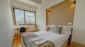 A bedroom with a bed, a desk, and a window with a view of buildings. - Legacy Oporto Premium Apartment I by Vacationy (Porto)