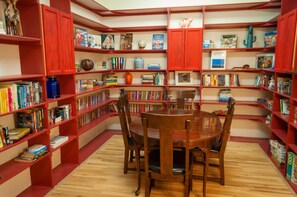 Una biblioteca con estanterías rojas, una mesa de madera y sillas.