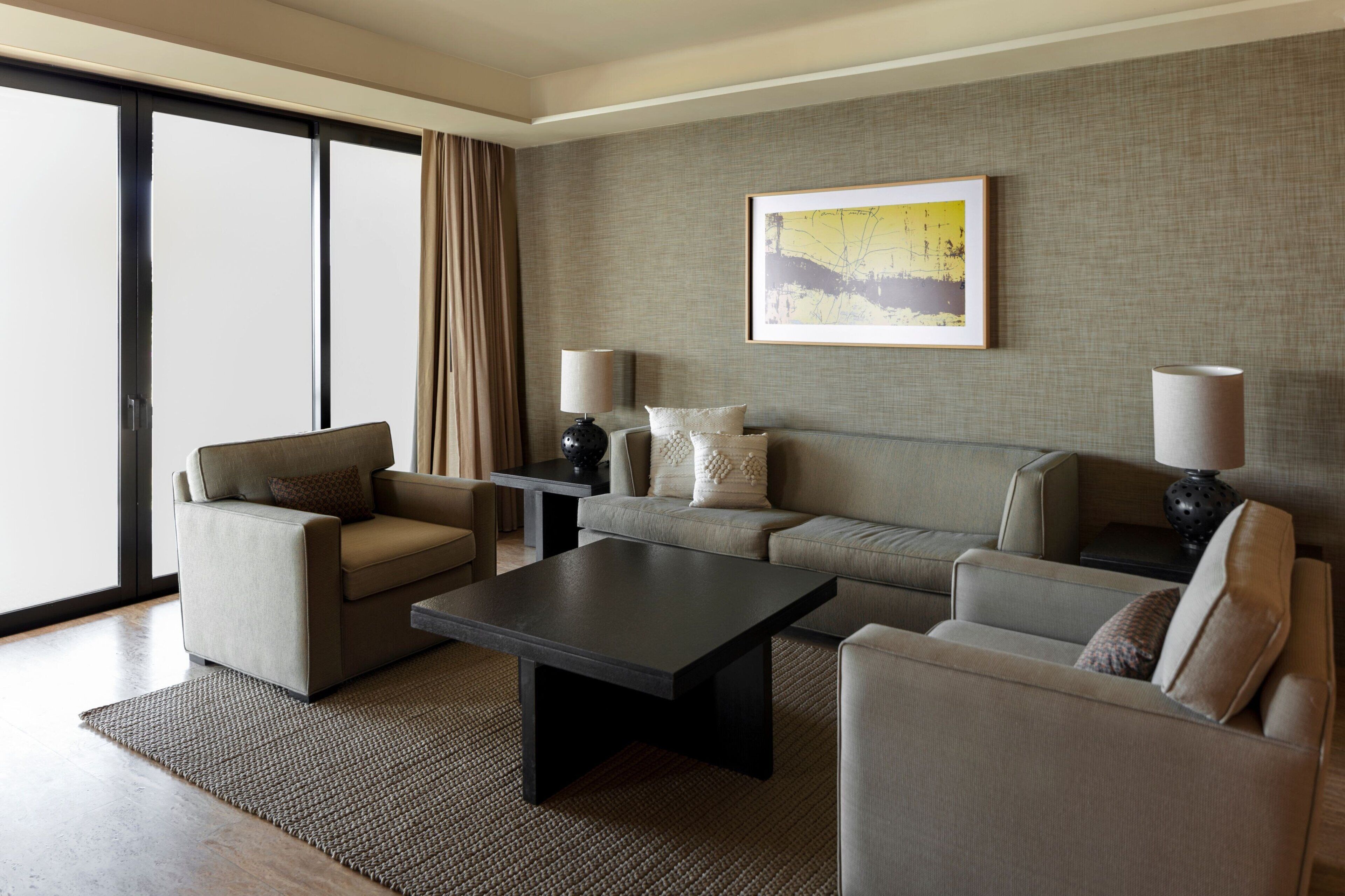 A modern living room with a sofa, two armchairs, a coffee table, and a large window with curtains.