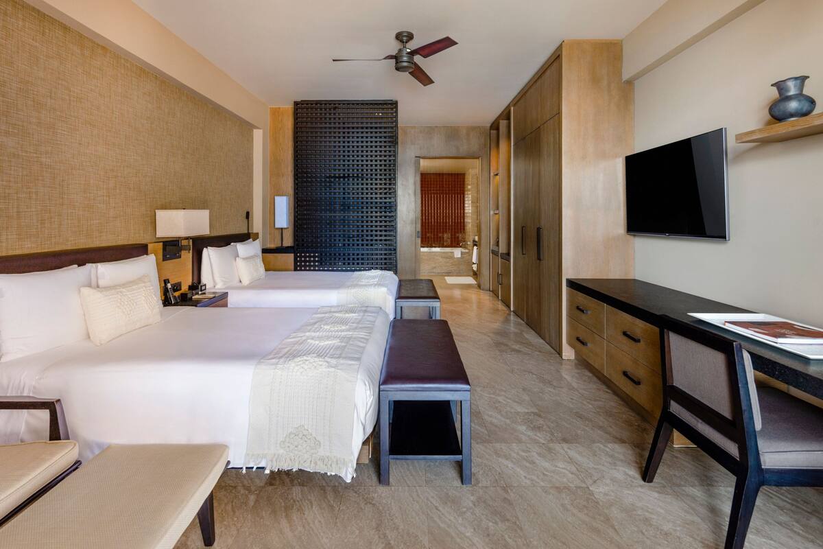 Une chambre d’hôtel avec deux lits, un bureau, une chaise, une télévision et un ventilateur de plafond.