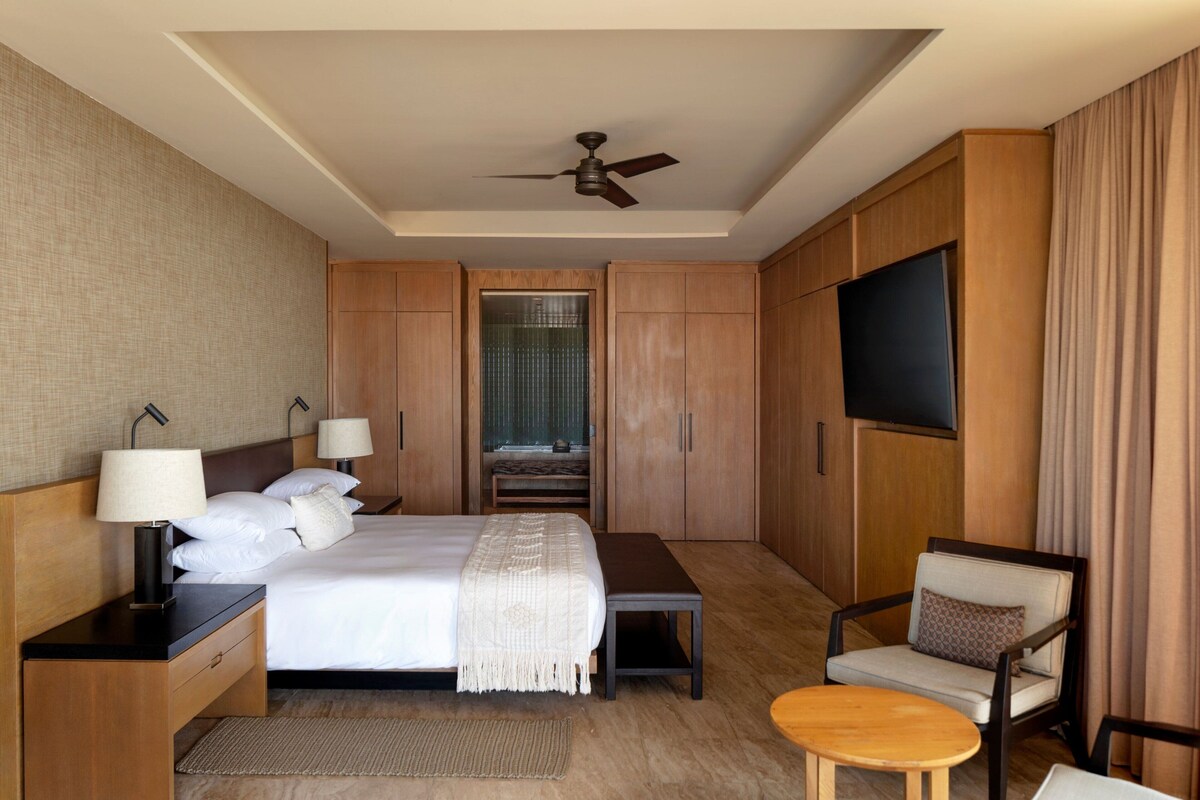 A hotel room with a bed, bedside tables, a TV, a chair, and a ceiling fan.