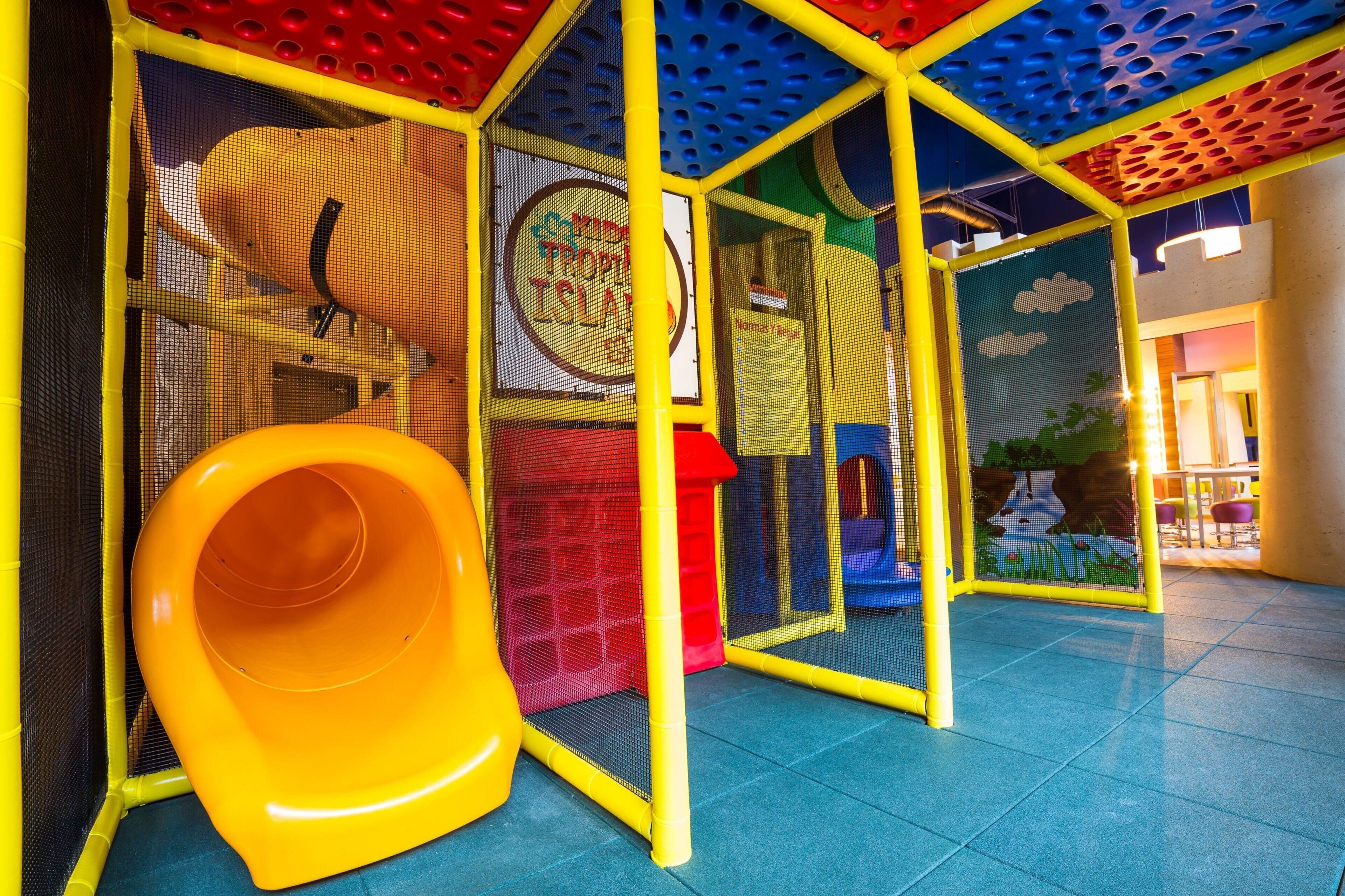 Zona de juegos con un tobogán amarillo y estructuras de juego cubiertas de red.