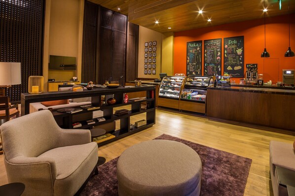 A modern hotel lobby with a seating area, a counter with a display case, and a menu board. - Casa Maat At JW Marriott Los Cabos Beach Resort & Spa (San José del Cabo)