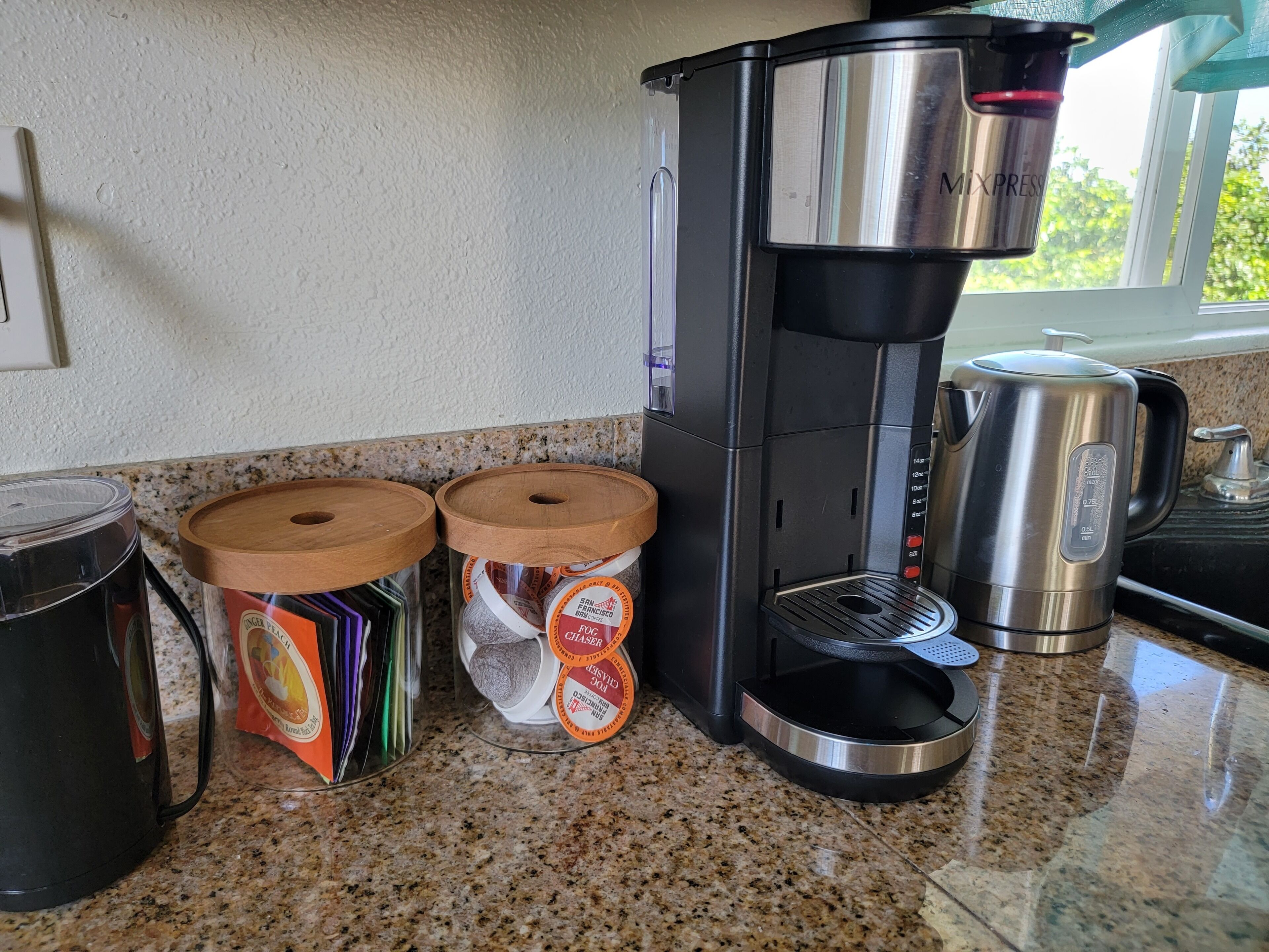 Una cocina con cafetera, dos frascos de especias y hervidor sobre una encimera de granito.