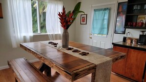 Une table de salle à manger en bois, agrémentée d’un chemin de table tissé, de bancs et d’un arrangement floral décoratif en guise de centre de table.