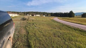 A rural landscape with a winding road, a parked vehicle, and a cluster of buildings in the distance. - The Air Bee-N-Bee: In The Heart of the Black Hills (Custer)