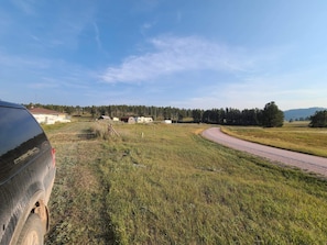 Paisagem rural com estrada sinuosa, um veículo estacionado e um conjunto de edifícios ao longe.