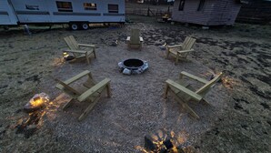 A campsite with a fire pit surrounded by wooden chairs, a trailer, and a small cabin. - The Air Bee-N-Bee: In The Heart of the Black Hills (Custer)