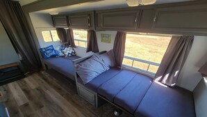 A compact RV interior with two sleeping areas, a kitchenette, and a window providing a view of the outdoors. - The Air Bee-N-Bee: In The Heart of the Black Hills (Custer)