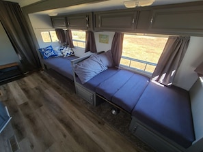 Interior compacto de uma RV com duas áreas de dormir, uma kitchenette e uma janela com vista para o exterior.