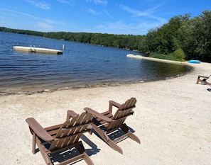 Hiekkainen ranta, jolla on kaksi puista Adirondack-tyylistä aurinkotuolia, ja ne ovat käännettyinä järvelle päin.