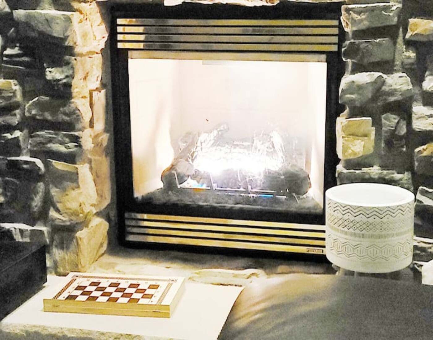 A fireplace with a chessboard and a decorative mug on a stone wall.