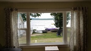 Ein Zimmer mit großem Fenster und Blick auf einen See, einem kleinen Tisch und einem Sessel.
