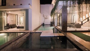 A modern outdoor pool area with glass walls, a lounge area with seating, and a staircase leading to an upper level. - Free Rooms!   Seminyak Bali Modern Walk to Beach Shopping New and Clean (Bali)