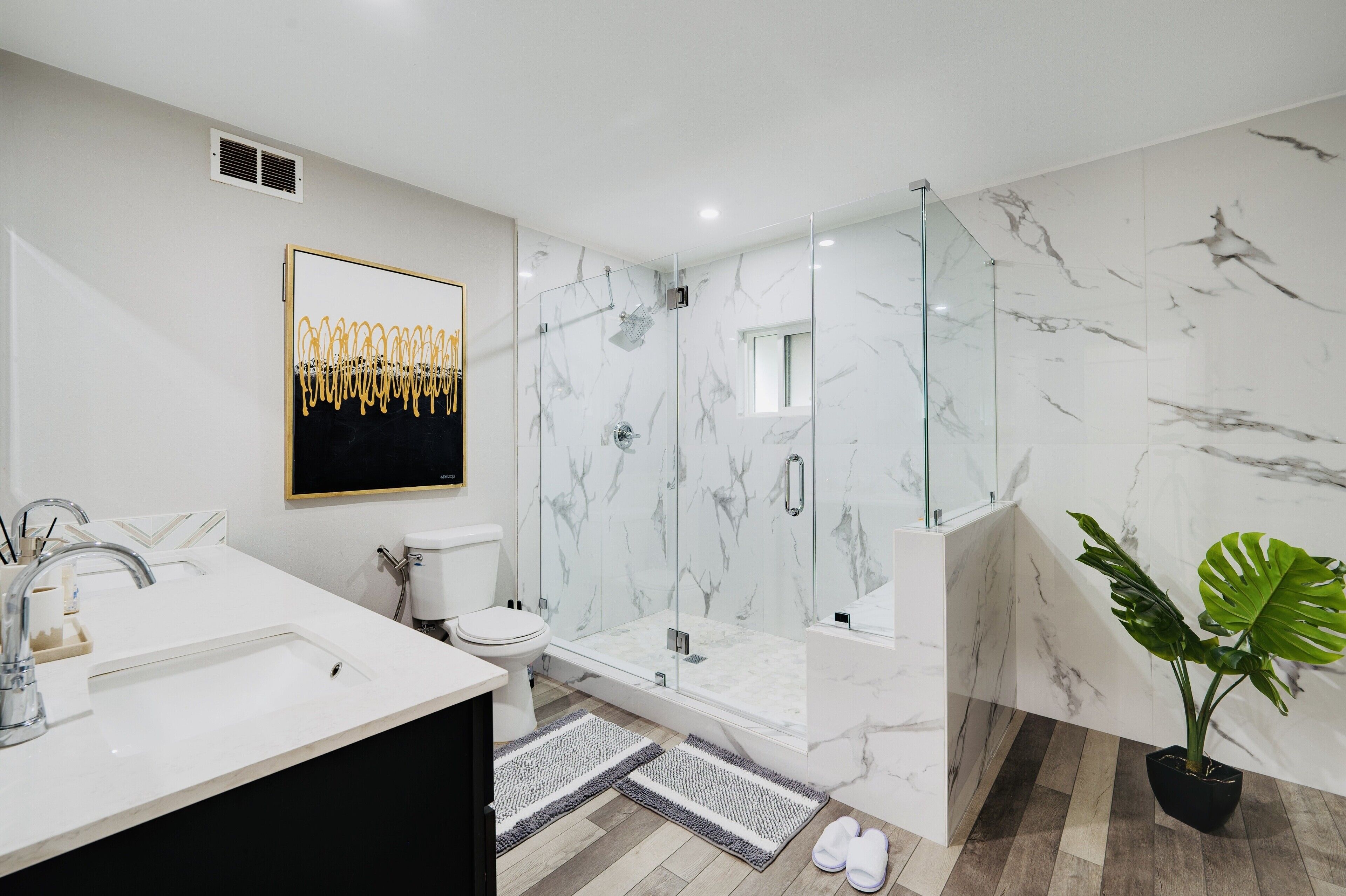 A modern bathroom with a glass-enclosed shower, a white sink, and a marble wall.