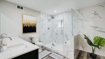 A modern bathroom with a glass-enclosed shower, a white sink, and a marble wall.