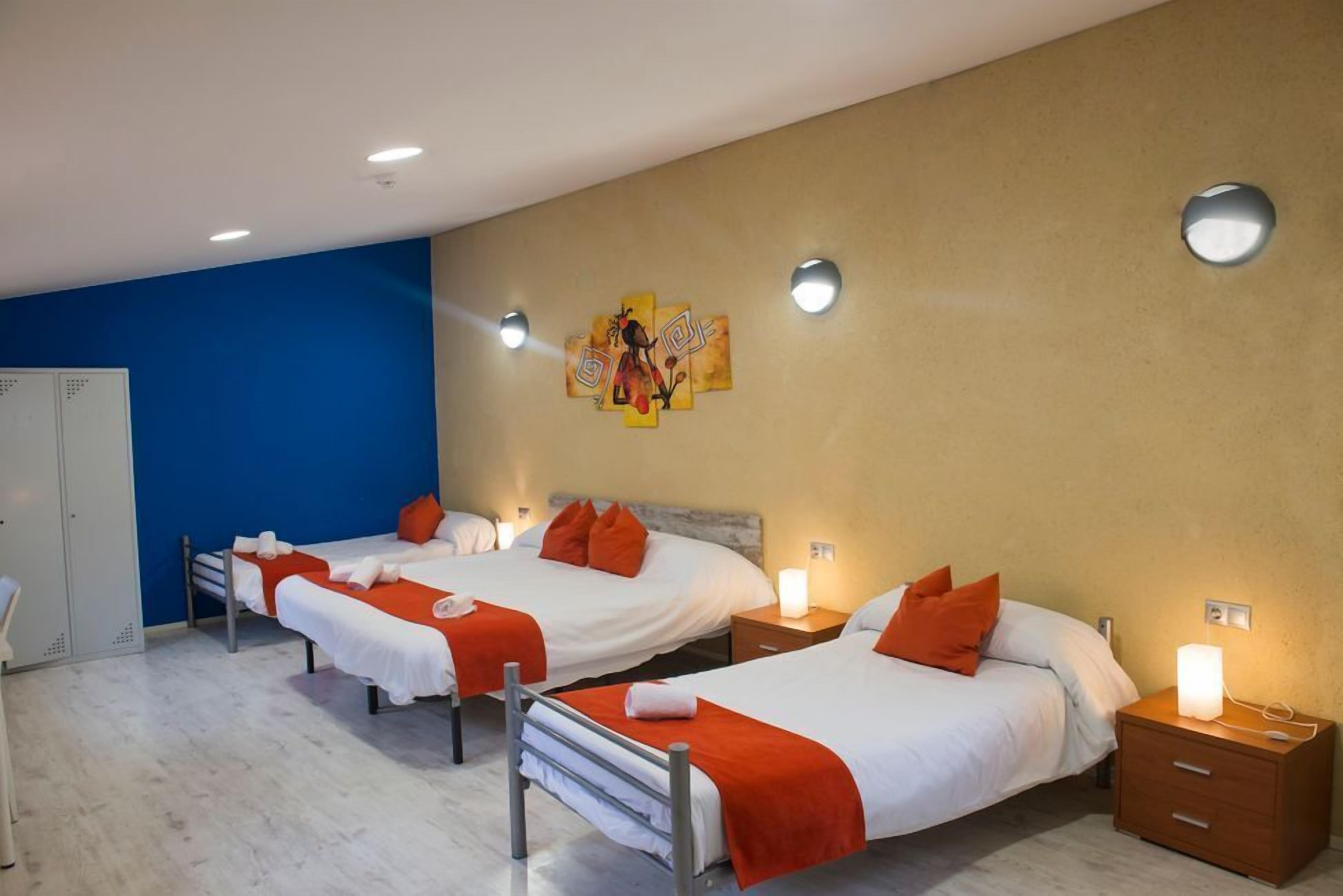 Habitación de hotel con dos camas individuales, cada una con una mesita de noche y una lámpara, un armario y una obra de arte colgada en la pared.