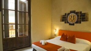 Ein Hotelzimmer mit einem großen Bett, orangefarbener Bettwäsche, einem Wandbild und einem Fenster mit Blick.