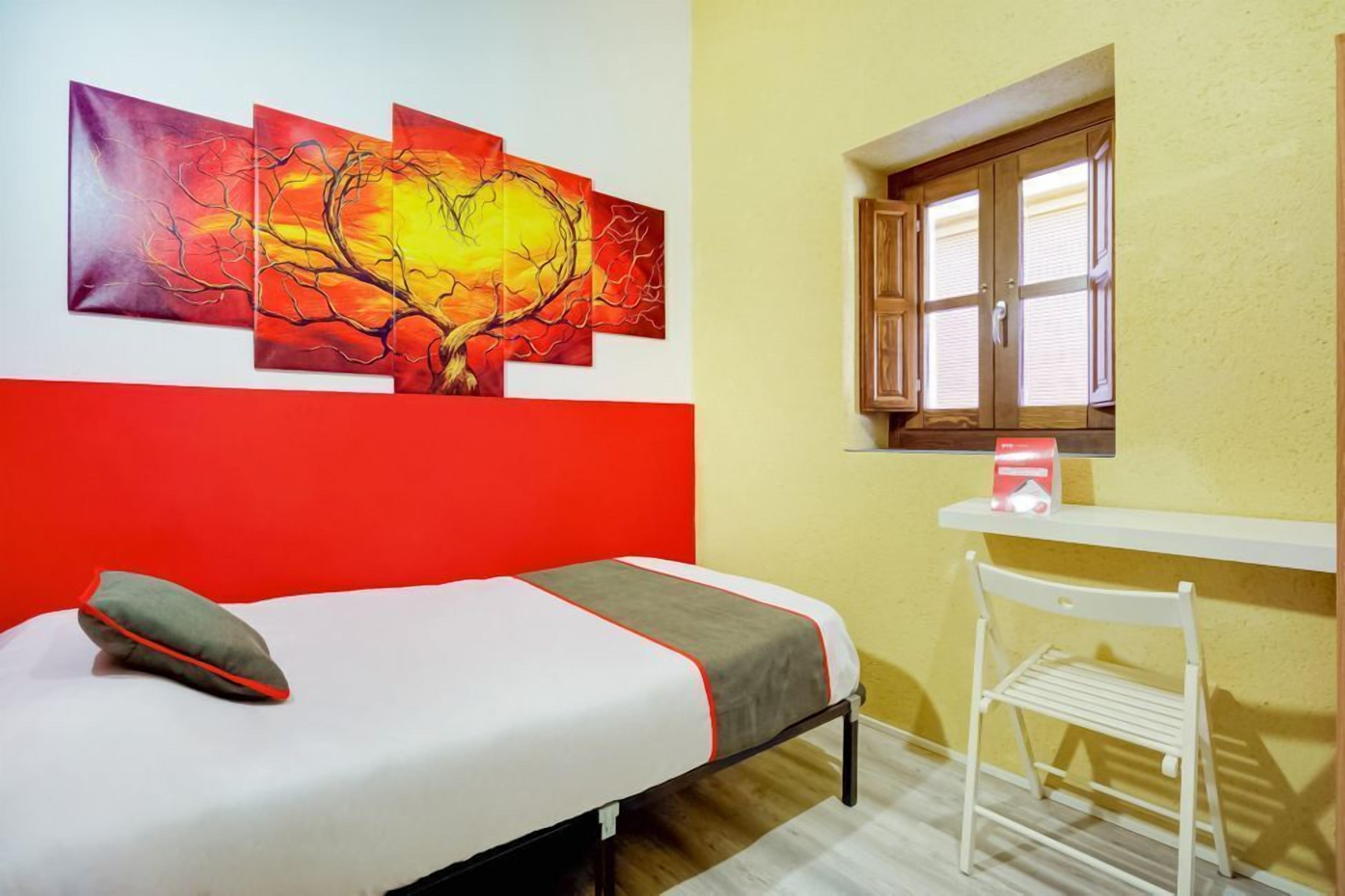 Een kamer met een bed, een bureau en een raam. Drie schilderijen hangen aan de muur.