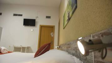 A hotel room with a bed, a television mounted on the wall, a door, and a wall-mounted light fixture.