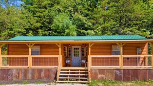 Una cabana de fusta amb teulada verda, un porxo amb dues cadires i una tanca metàl·lica que envolta la propietat.