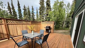 Um deck de madeira com mesa e cadeiras, cercado por um cercado de madeira e árvores.