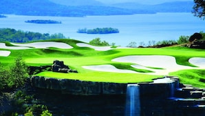 Ein Golfplatz mit Sandbunkern, einem Wasserfall und einem See im Hintergrund.