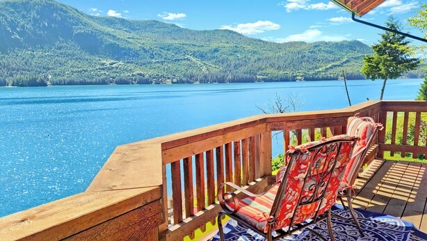 A wooden deck with a view of a lake and mountains. There are two chairs with patterned cushions. - Private 2 bedroom Oceanfront Oasis with Panoramic views! (Craig)