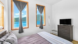 A bedroom with a bed, two windows with curtains, a dresser, and a television. - Private 2 bedroom Oceanfront Oasis with Panoramic views! (Craig)