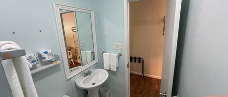 A bathroom with a sink, mirror, and toilet. There is a towel rack with towels and a small shelf with toiletries.