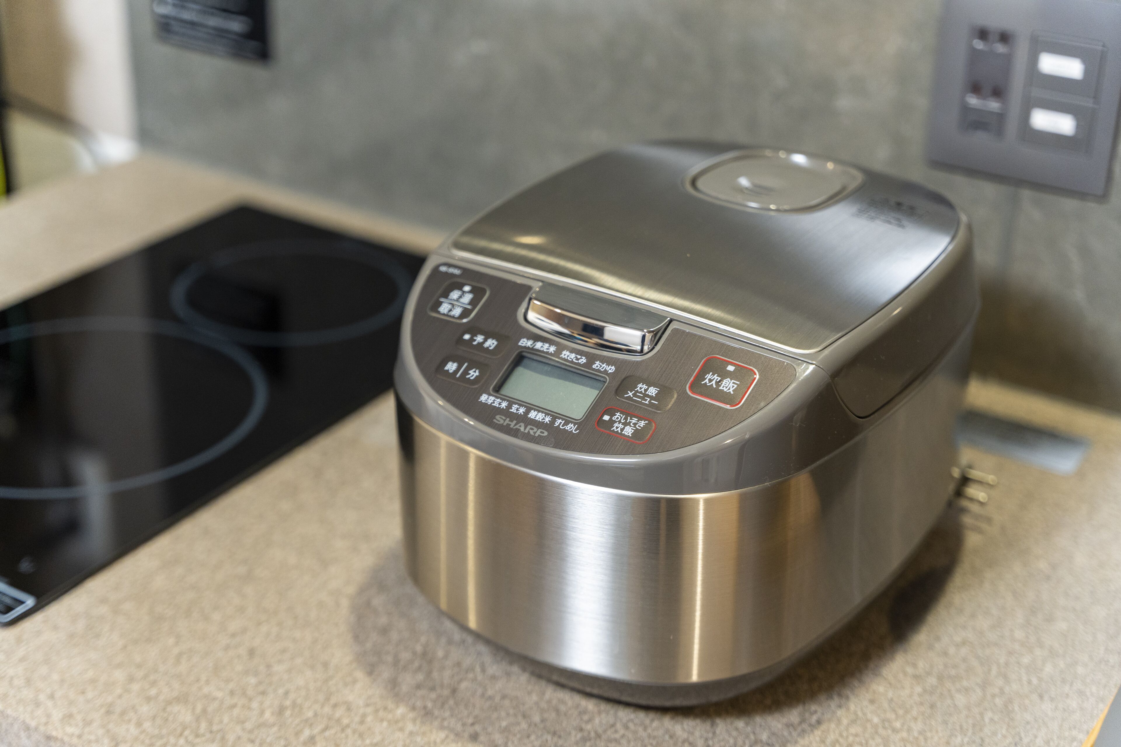 A stainless steel rice cooker with a digital display and control panel, placed on a kitchen countertop.