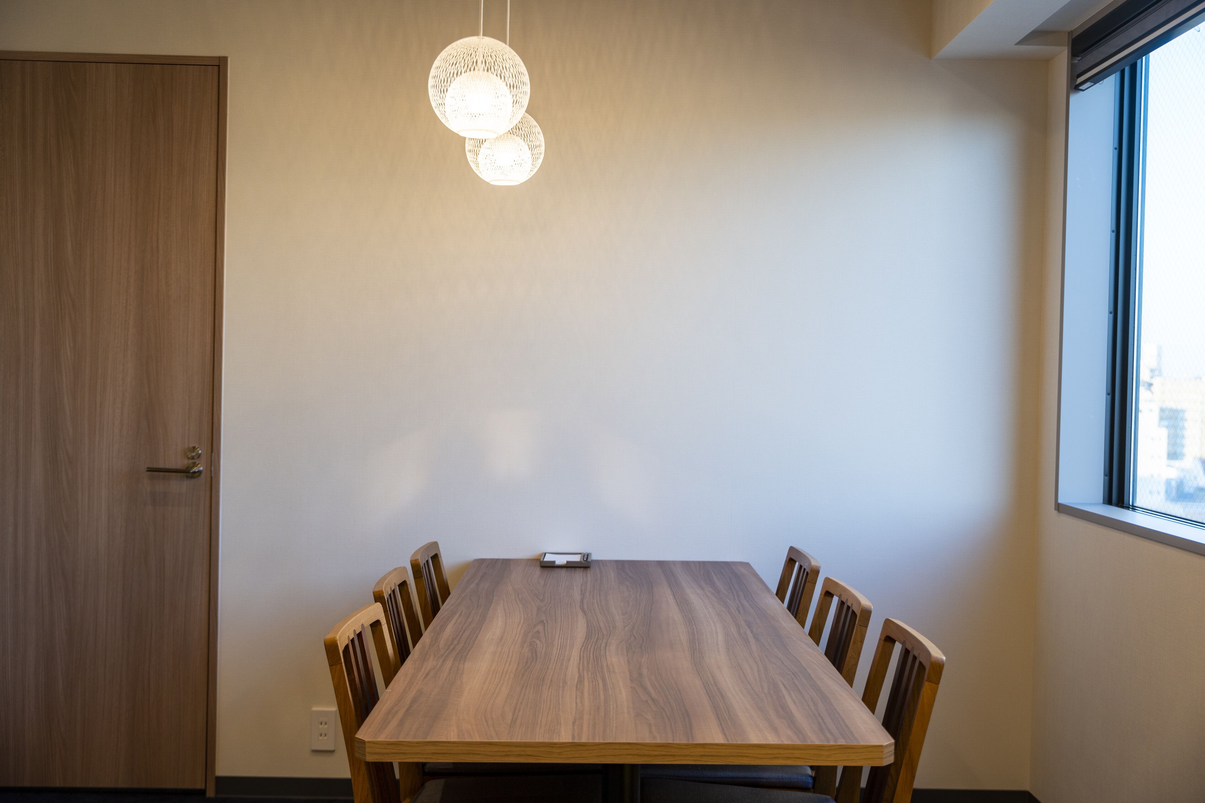 Una sala de conferencias con una mesa de madera, sillas, una lámpara colgante y un ventanal con vistas.