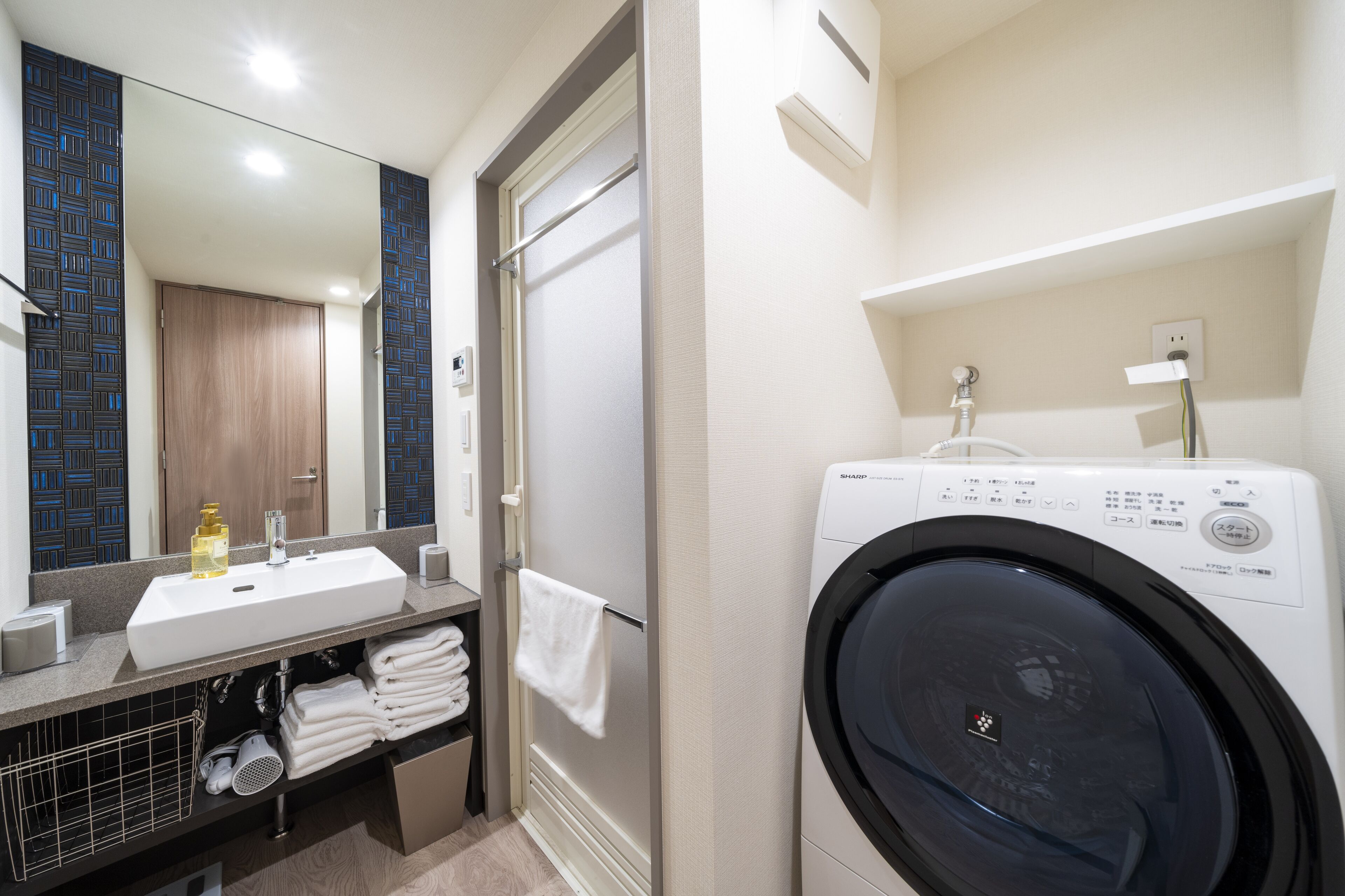 Une salle de bain moderne équipée d’un lave-linge intégré, d’un lavabo avec miroir et d’un porte-serviettes.