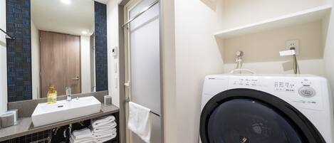 Une salle de bain moderne équipée d’un lave-linge intégré, d’un lavabo avec miroir et d’un porte-serviettes.