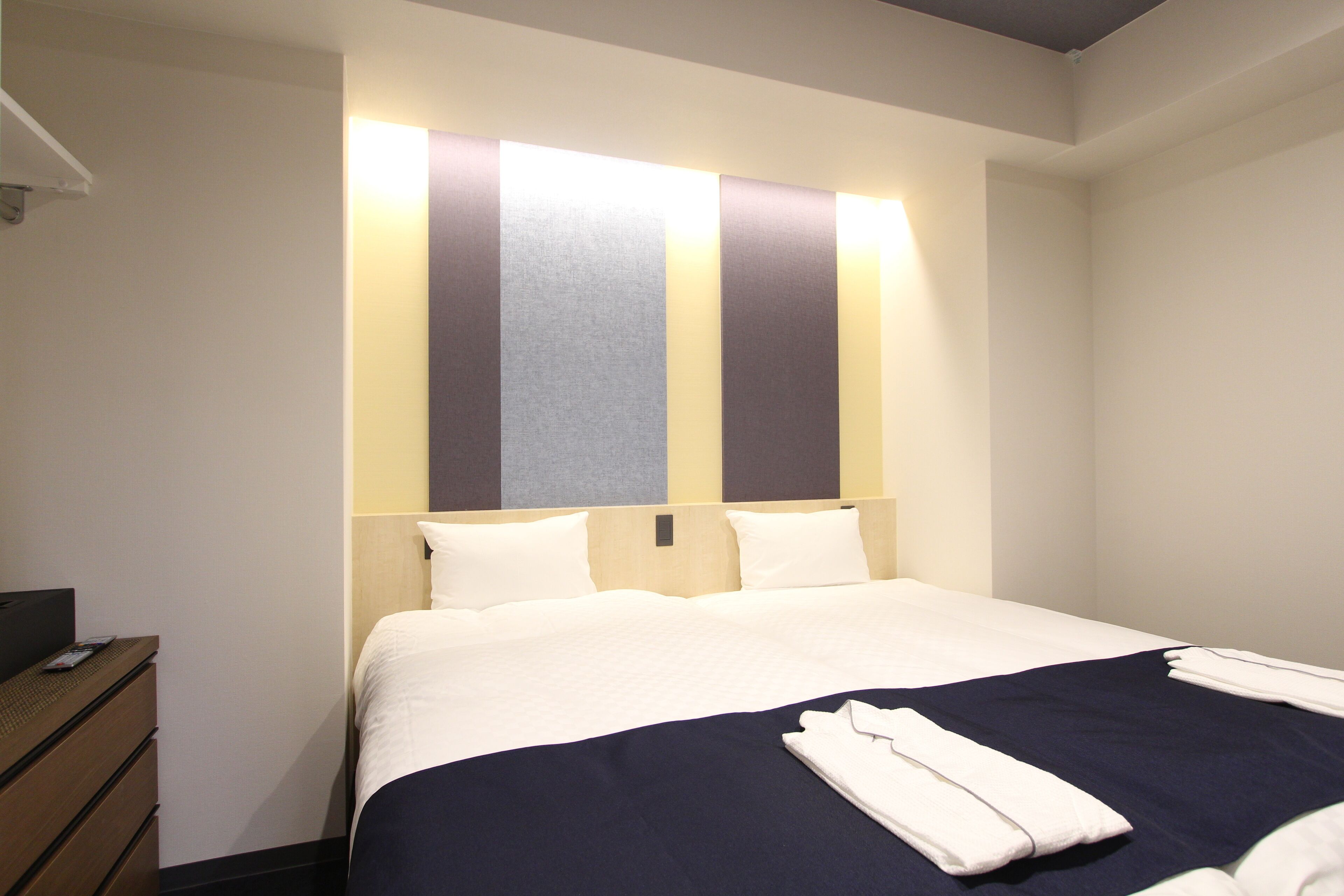 A hotel room with a bed, a wooden dresser, and a wall-mounted light fixture.